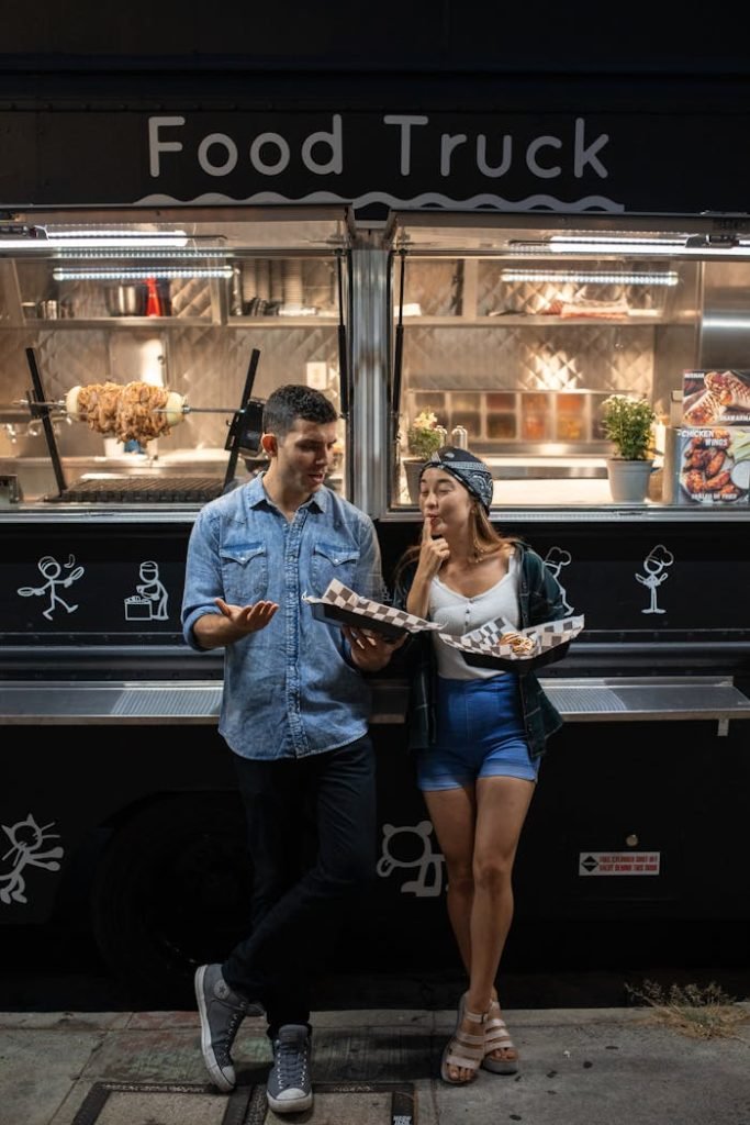 Urban couple savoring meals at night by a trendy food truck, showcasing street food culture.